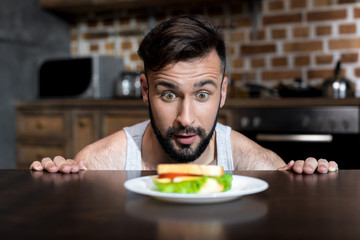 close-up view of hungry bearded young man looking at breakfast on kitchen table