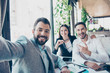 © deagreez - Happy friends business partners are making selfie photo, sitting in the terrace of the restaurant. They are posing, smiling and gesturing, all wearing formal smart outfits