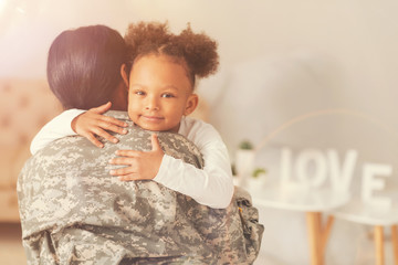 Cute curly girl hugging her mother in military uniform