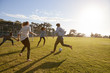 Four young adults playing football in a park at sunset