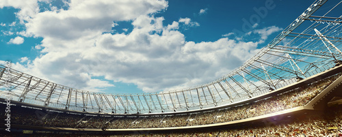 Zdjęcie XXL zatłoczony stadion piłkarski z trybunami na niebieskim tle pochmurnego nieba