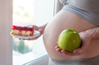 © Artem - Pregnant woman belly holding a plate with junk and healthy food. Concept choice of diet during pregnancy