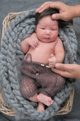 .cute asian boy newborn portrait  with white doll one month lie down  on grey background fabric in basket with hands of his dad .