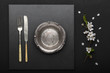 Beautiful empty plate with knife and fork with spring blooming branch on black table. Flat lay, top view.