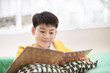 © sirikorn - Happy Asian boy reading story book on the sofa
