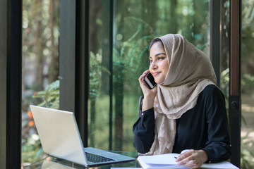 Muslim lady is busy on the phone at her desk.