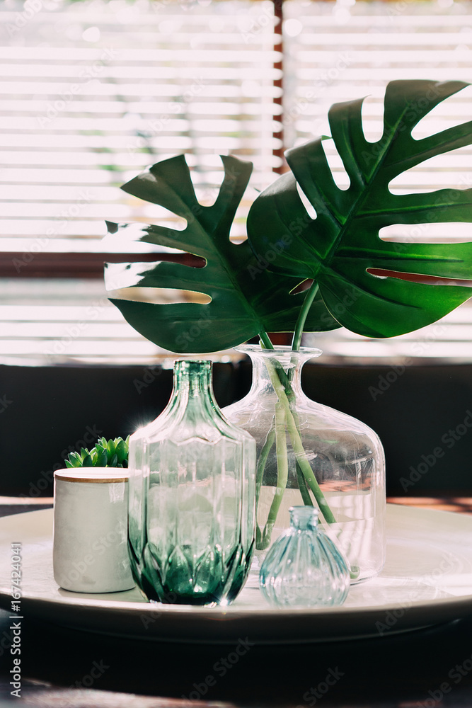 Monstera palm leaves in a vase on a dining table with vintage objects ...