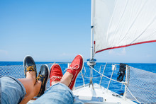 Two pairs legs in red and blue topsiders on white yacht deck. Yachting