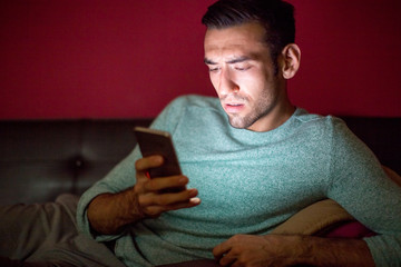worried man using smartphone on sofa at night