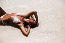 Beautiful Stylish Sexy Woman Lies On The Seashore, Ocean, Enjoys The Sun, In White Knitted Bikini, Modern Turkish Woman, Long Dark Hair, Healthy Shining Bronze Skin, Perfect Figure, Tropical Lifestyle