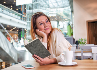 Wall Mural - Relaxed smiling girl reading book in cafe at shopping mall