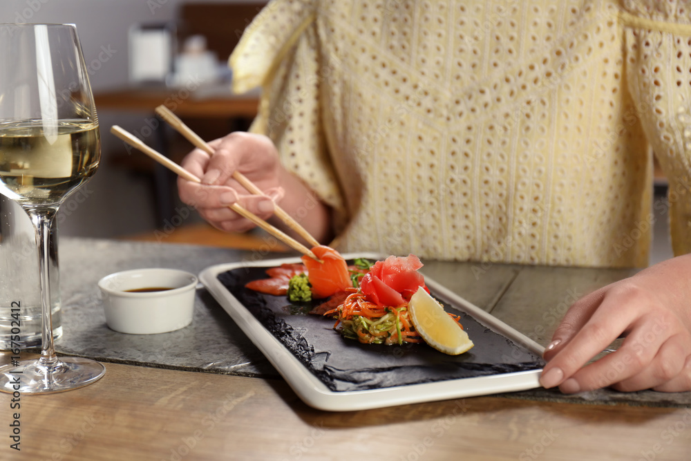 Woman holding delicious salmon slice with chopsticks at table