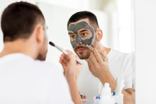 Young Man Applying Clay Mask To Face At Bathroom