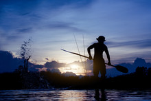Silhouette Of  Fisherman Standing On Boat,hold Paddle And Paddle With A Splash Of Water On Sunset Background.