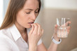 © fizkes - Unhealthy woman with pained facial expression feels unwell, suffering from migraine headache, takes pill analgetic medication to relieve pain, stressed lady holds tablet and glass of water, headshot
