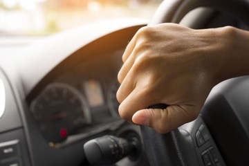 Driver's hands on the steering wheel inside of a car with beautiful green forest perspective, road trip travel concepts.