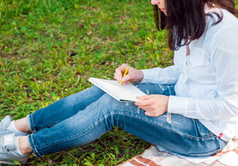 Young beautiful girls drawing the pictures in sketchbook. At the park