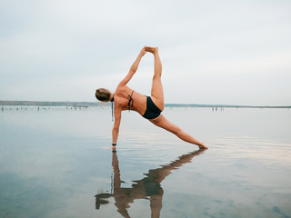 Young caucasian woman in swimsuit practicing yoga in water liman, lake or river. Beautiful reflection. Complex asanas, balance. Fitness, sport, yoga and healthy lifestyle concept.