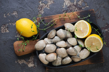 Metal plate with raw fresh vongole clams on a wooden chopping board, brown stone background, flat-lay