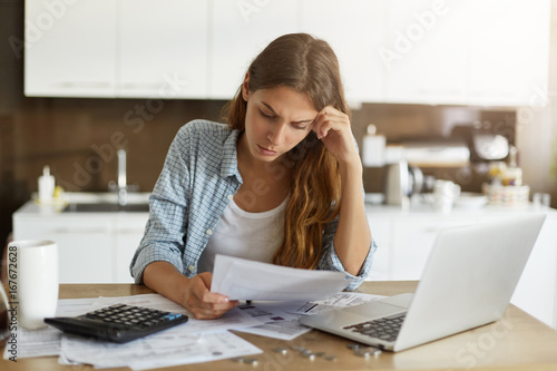 Fotomural Attractive young housewife wearing shirt at home studying gas and electricity bi
