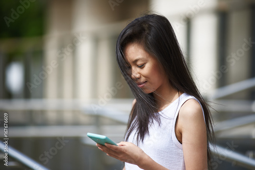 Outdoor Portrait Of Brunette Korean Girl Typing Text Message