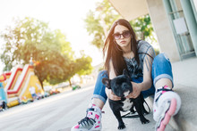 Urban Portrait Of Beautiful And Attractive Girl With  French Bulldog And Sunglasses. Warm Summer Colors And Haze. Strong Back Light.