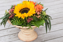 Autumn Flowers In Pot.
Arrangement With Sunflower, Orange Roses, Limonium , Hypericum And Green Leaves.