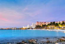 High Rise Hotel Area In Aruba At Dusk. Palm Trees In Motion Suggest The Windy Weather, A Well Known Characteristic Of This Island, Located On The Southern Fringes Of The Caribbean
