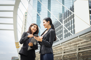 two business woman standing using smartphone and discussing in front of the office. business working