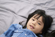 © kornnphoto - closeup Asian children cute or kid girl wearing jeans with sleeping or sleepy and open eye with white teeth smile on gray bed and bedtime in bedroom at home on warm white with space