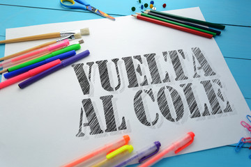 Wall Mural - The text Back to school (Spanish language) on a sheet of paper on the table with school accessories (pens, pencils, brushes)