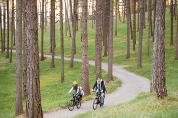 Wall Mural - Young family in warm clothes cycling in autumn park