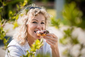 Mature woman bitten donut. Junk-food concept.