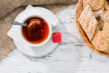 Canvas Print - cup of tea and basket with cookies served for breakfast on wooden table, top view