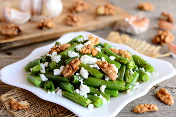 Warm green beans salad with cottage cheese and walnuts on a white plate and old wooden table. Rustic style. Easy green beans recipe idea. Closeup