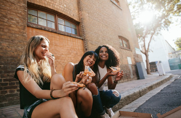 Wall Mural - Beautiful girls sitting outdoors by the road eating pizza