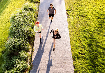 Canvas Print - Group of young athletes running in green sunny park.