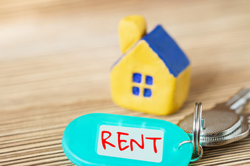 Miniature yellow toy house with keys and inscription RENT on the wooden surface. Property and real estate concept. Selective focus