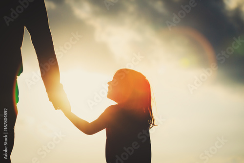 Fotografie, Obraz silhouette of little girl holding parent hand at sunset