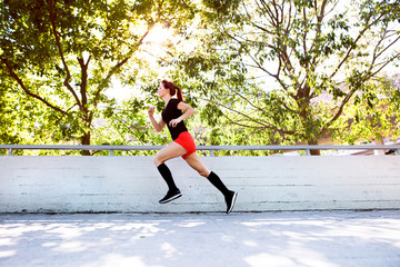 Sticker - Beautiful young athlete running on a path in the city.