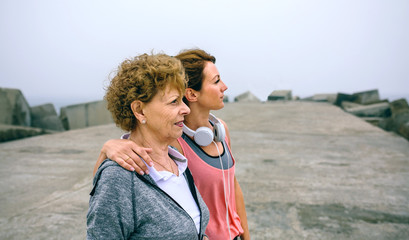 Wall Mural - Senior and young sportswoman looking away by sea pier