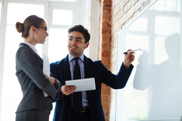 Sticker - Young economist pointing at whiteboard while explaining statistics to colleague