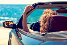 Beautiful Blond Smiling Young Woman In Convertible Top Automobile Looking Sideways While Parked Near Ocean Waterfront