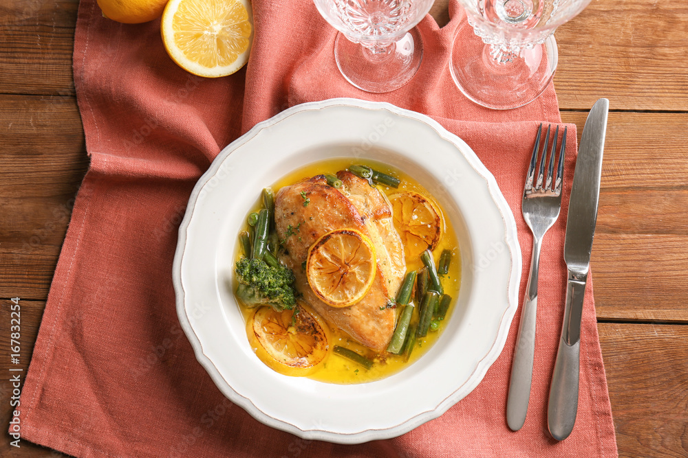 Delicious chicken breast with lemon and vegetables in plate on table