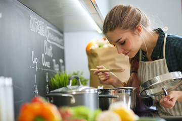 Young woman standing by the stove in the kitchen .