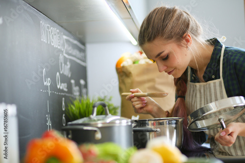 Fotomural Young woman standing by the stove in the kitchen .