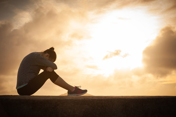 Sad young woman with her head down sitting outdoors.