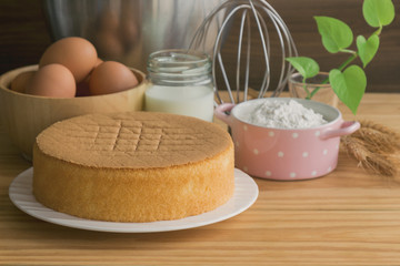 Homemade sponge cake on white plate.Soft and lite delicious sponge cake with ingredients: eggs flour milk on wood table. Homemade cake with ingredients in homemade bakery concept for bakery background