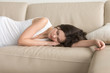 Young woman lying asleep on couch, sleeping attractive girl taking nap at home, resting on arm on comfortable sofa, exhausted teenager dozing after sleepless night, feeling lack of sleep deprivation