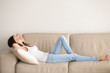 © fizkes - Young woman lying on couch cushion with eyes closed, relaxing on cozy sofa pillow, relaxed girl taking nap at home hands behind head, breathing fresh air, no stress, enjoying day off in living room